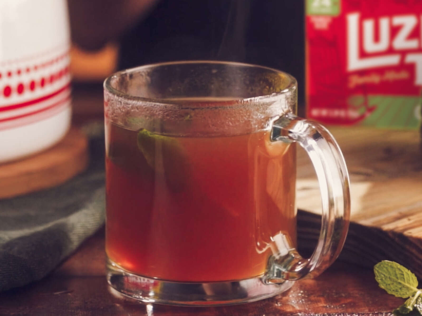 A warm glass mug of tea garnished with mint and served with honey